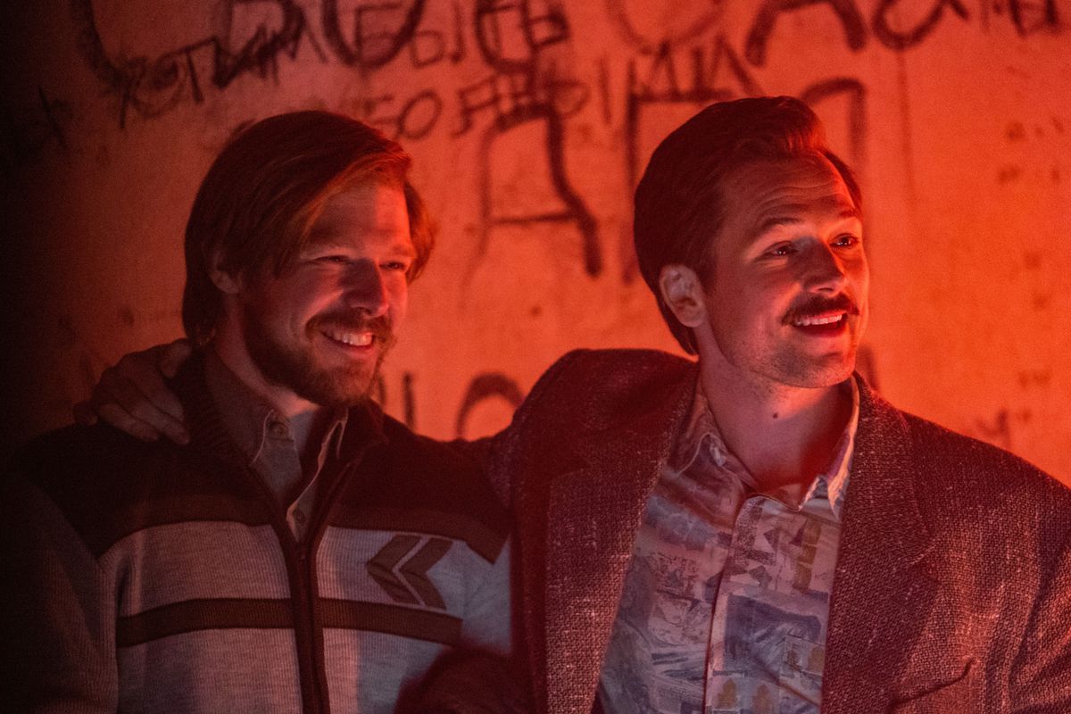 Alexey Pajitnov (Nikita Efremov) and Henk Rogers (Taron Egerton) embrace and smile, standing in front of a graffiti-covered wall, bathed in red light