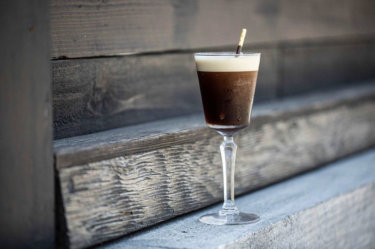 A close up shot of a chocolate-y cocktail with foam top on wooden board.