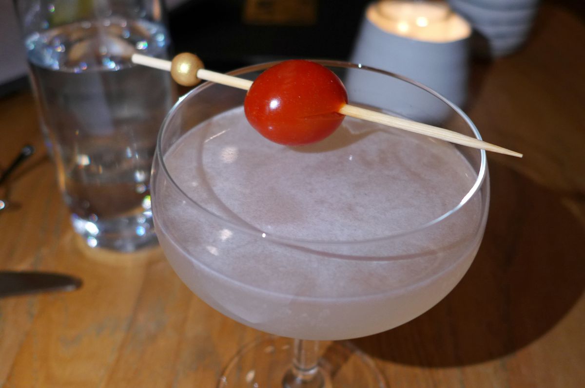 A martini glass with a milky white fluid and tiny plum tomato on a toothpick.