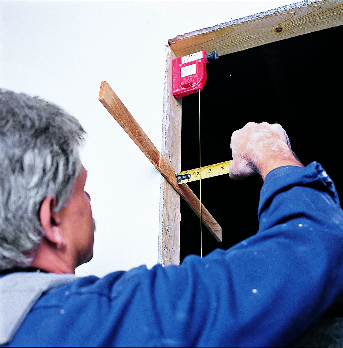 Man Taking Measurements With Plumb Bob To Place Shims