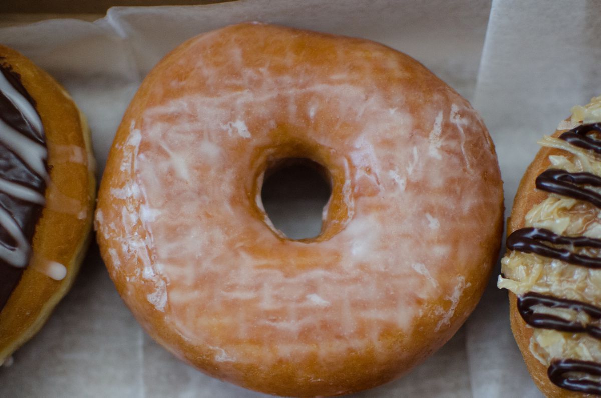 Closeup overhead shot of a honey dip doughnut. Two different doughnuts are visible on the edges of the photo, one on each side of the honey dip.
