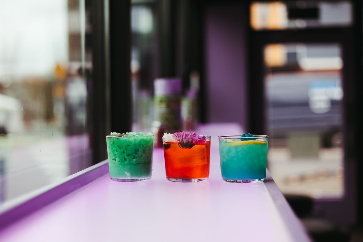 Seafoam green, red, and blue cocktails sit on the purple standing bar of Toyshop Ramen.