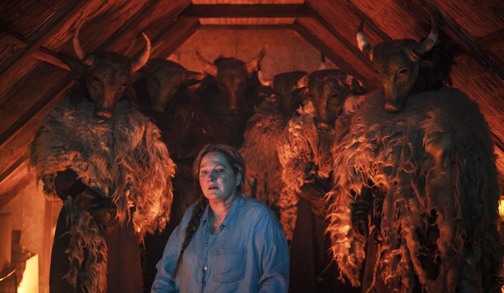 A woman stares transfixed as she is surrounded by a group of mysterious masked figures in a cramped cabin in Moloch.