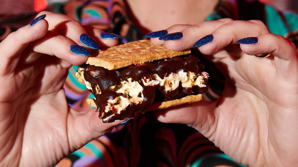 Two hands hold a graham cracker sandwich filled with marshmallows and chocolate.