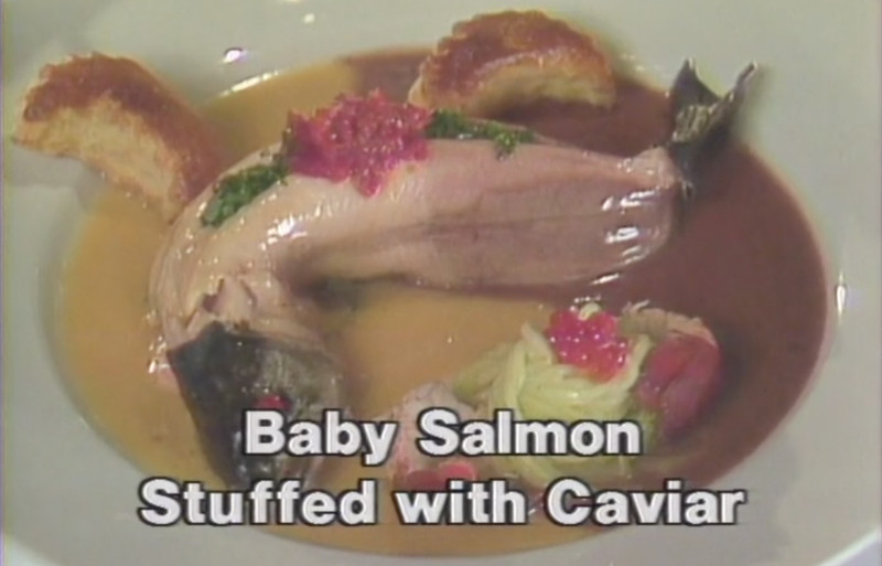 Caption “Baby Salmon Stuffed With Caviar” appears over a still of a dish of skinned salmon on a plate with broth, caviar, and a cabbage salad.