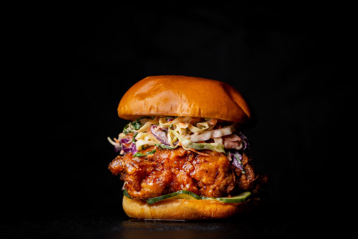 Hamburger buns around a stack of fried chicken, coleslaw, and pickles.