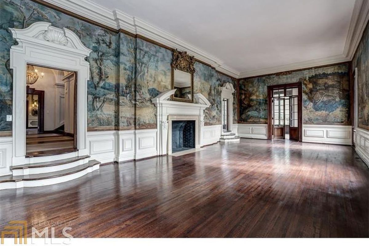 A large room with dark wood floors and soaring ceilings, with intricately painted pastoral murals and a large, grand fireplace.