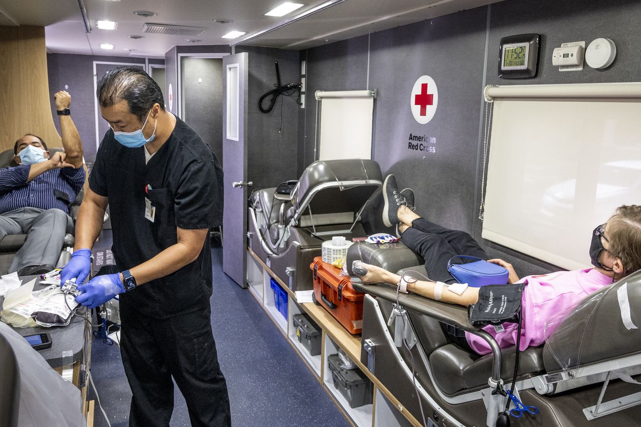A picture of the inside of a Red Cross bloodmobile as a nurse draws blood from two patients on either side of the vehicle.