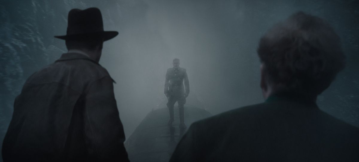 Indiana Jones (left) and Basil Shaw (right), with backs to the viewer, confront bad guy Jurgen Voller, silhouetted in mist, atop a moving train.