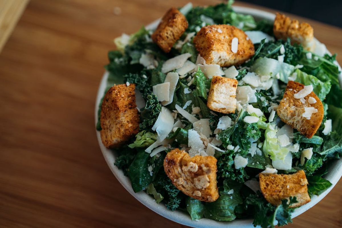 A salad with greens, croutons, and shaved white cheese.