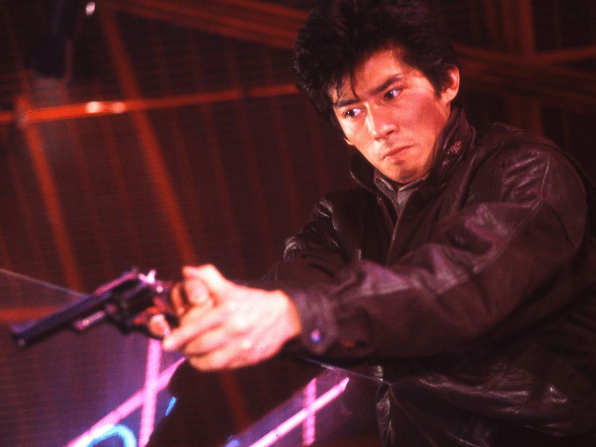 A young Hiroyuki Sanada wears a leather jacket and holds a revolver against a dark red background in Royal Warriors.