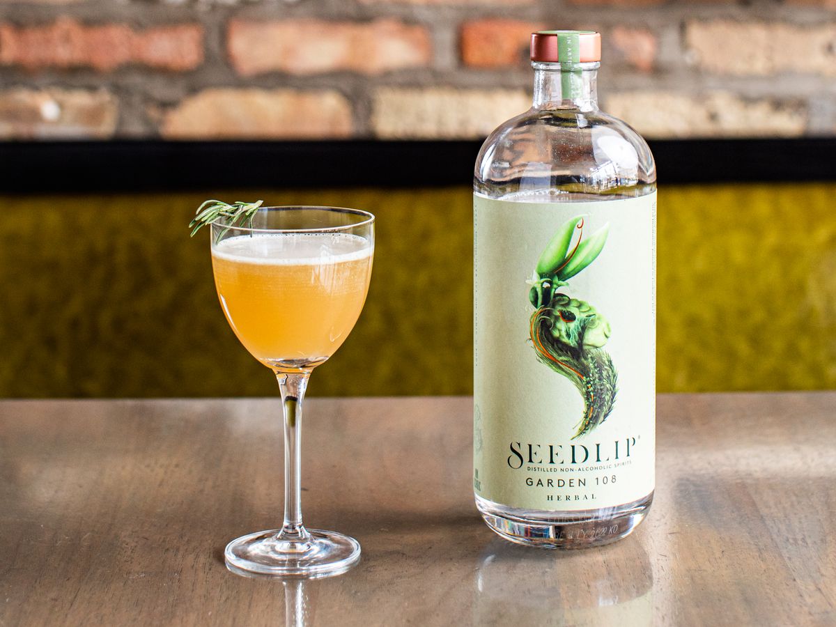 A bright yellow cocktail topped with herbs, and a glass bottle of Seedlip Garden 108.