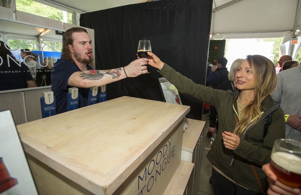 A brewer hands a beer to a customer.