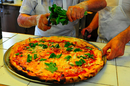Fresh basil being tossed atop a big pizza pie.