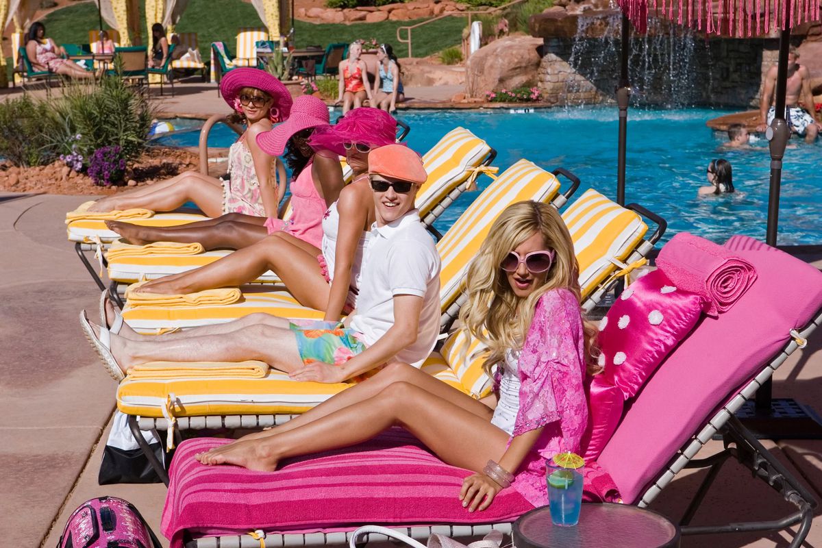 Ashely Tisdale as Sharpay Evans, on a lounge chair with her brother Ryan on an adjacent chair, and assorted female friends on subsequent poolside chairs.