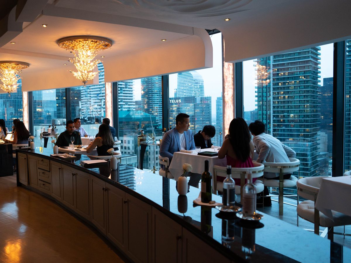 Diners seated in a luxe dining room with huge windows looking out at the high rise buildings of Toronto.