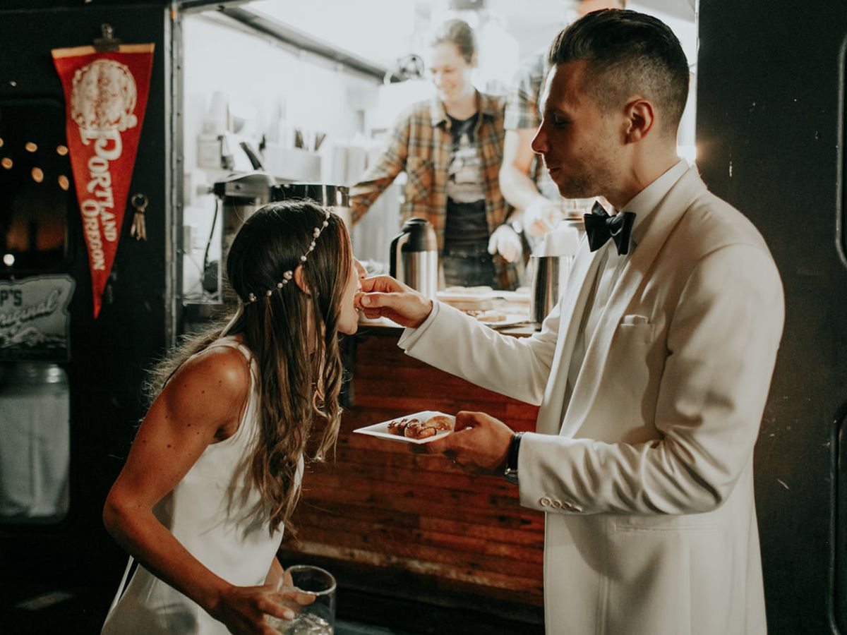 A man in a white suit feeds his new wife a mini doughnut from Pip’s Original in Portland.