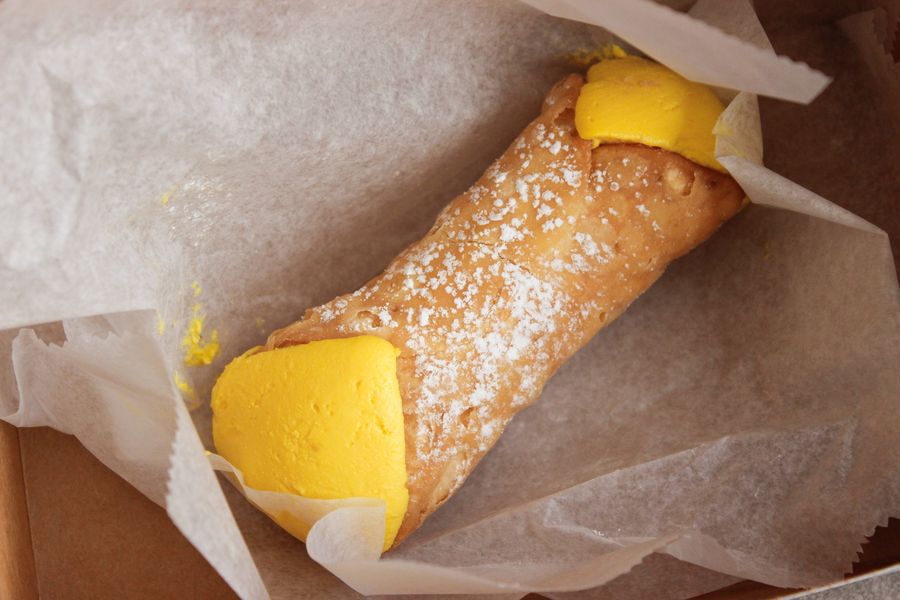 A single cannolo, stuffed with a yellow-colored cream, sits on tissue paper