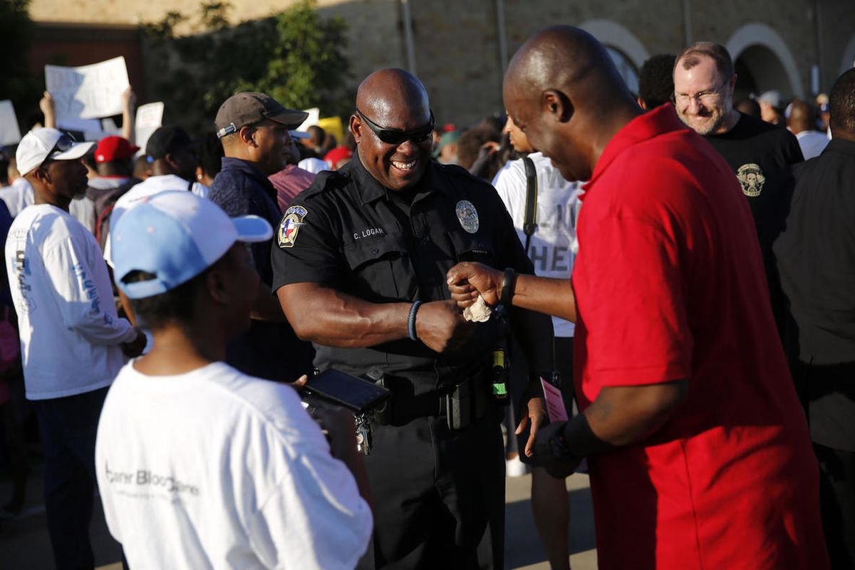 McKinney police officer Curtis Logan, center, receives a fist bump from Mark Matthews of North Dallas as the two attended the protest that started at Joyce Kelley Comstock Elementary, Monday June 8, 2015.  The group marched to the Craig Ranch pool where M