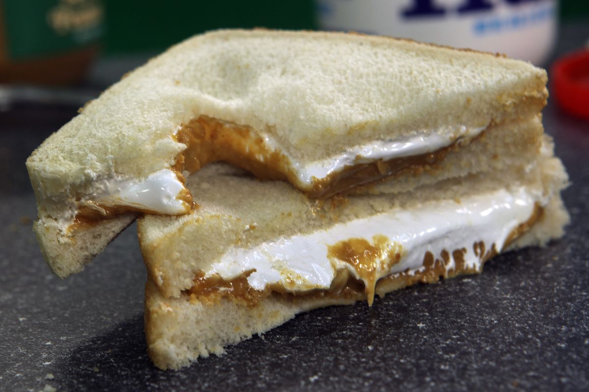 A sandwich on white bread is cut on the diagonal, with one half stacked on the other. It’s filled with peanut butter and marshmallow Fluff.