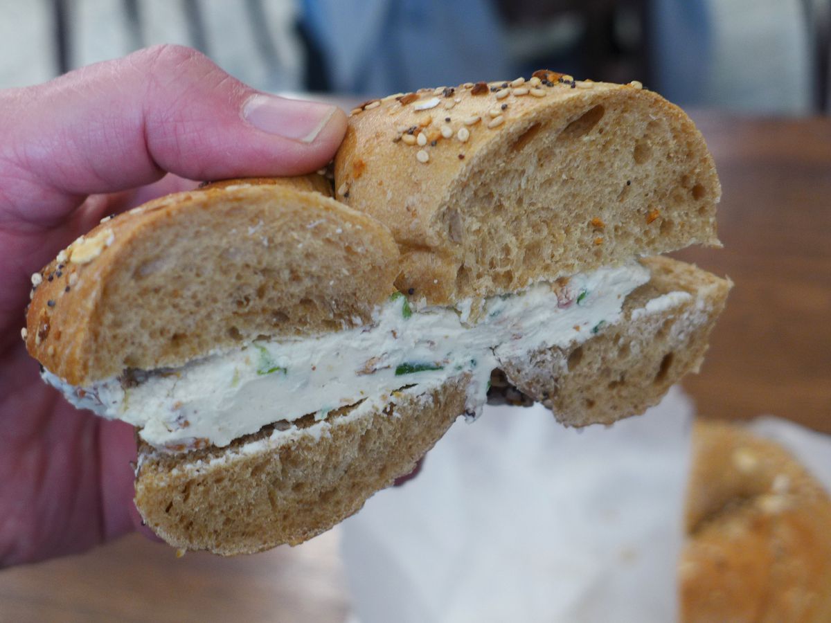 A half bagel held by a hand with the cream cheese threatening to ooze out.