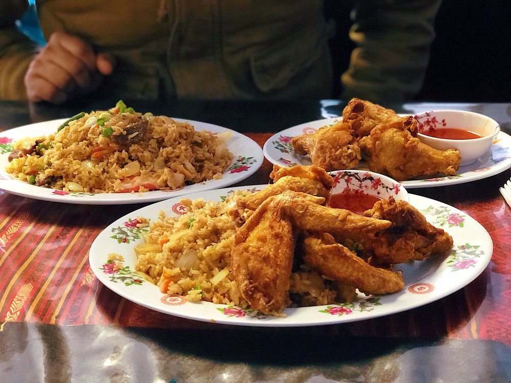 Three plates boast fried chicken wings, fried rice, and dipping sauces.