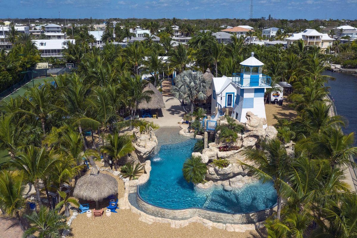 An aerial view of a resort-type pool, with palm trees and a blue and white lighthouse surrounding the water. 