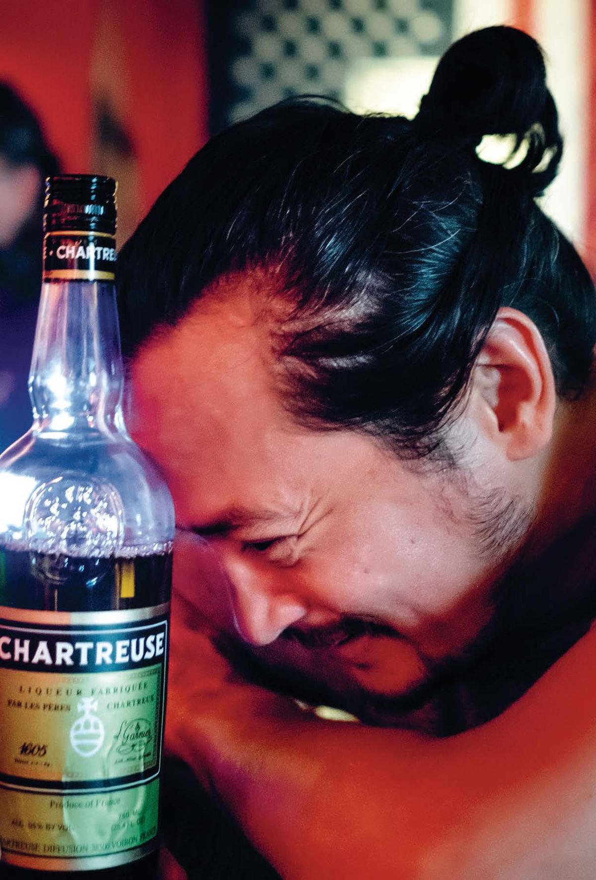 A man, Brendan Finnerty, leans his head against a bottle of Chartreuse. 
