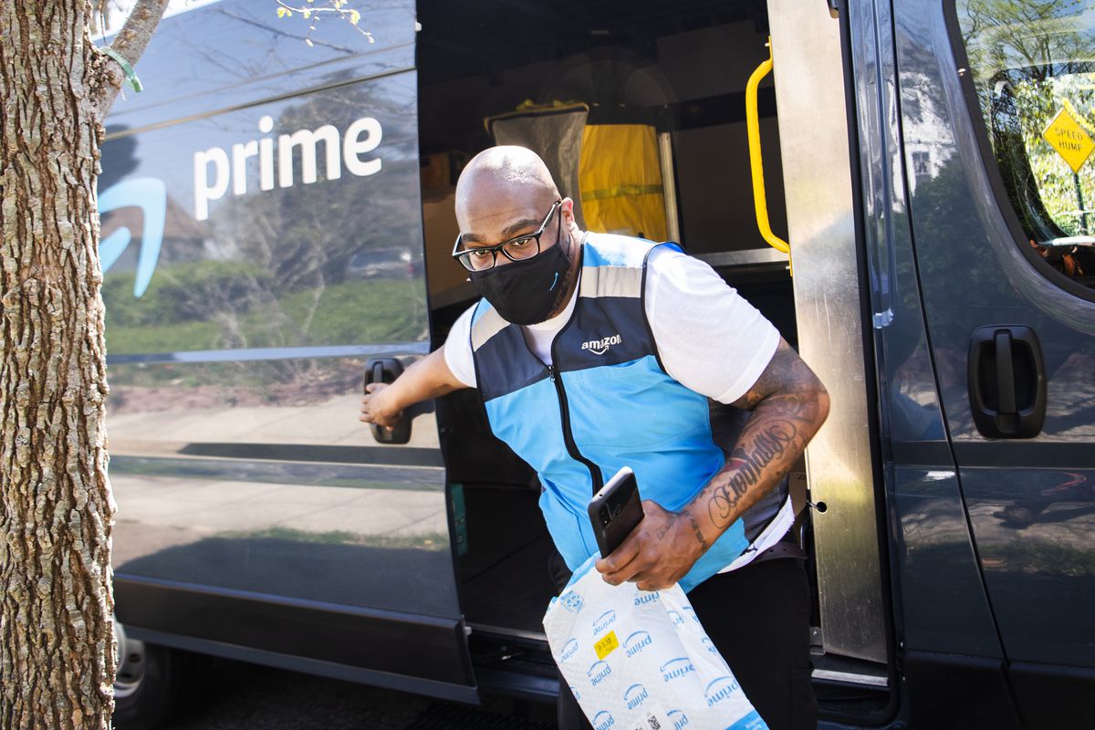 An Amazon delivery worker with packages coming out of an Amazon van.