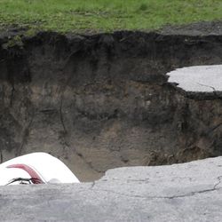 A section of a car can be seen in a gaping sinkhole that opened up a residential street on Chicago's South Side after a cast iron water main dating back to 1915 broke during a massive rain storm Thursday, April 18, 2013, in Chicago. The hole spanned the entire width of the road and chewed up grassy areas abutting the sidewalk. Two of the cars that disappeared inside had been parked, but a third was being driven when the road buckled and caved in. Only the hood of one of the vehicles could be seen peeking from the chasm.(AP Photo/M. Spencer Green)