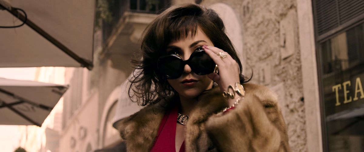 A woman in giant dark sunglasses and a fur coat tips her glasses down to look at something.
