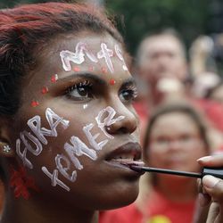 A demonstrator with the Portuguese words "Get out Temer" holds still for someone else applying lip gloss during protest demanding the impeachment of Brazil's President Michel Temer in Sao Paulo, Brazil, Sunday, Nov. 27, 2016. Protesters expressed outrage at a host of Temer's policies, including the government's proposal to cap spending to rein in the deficit. 