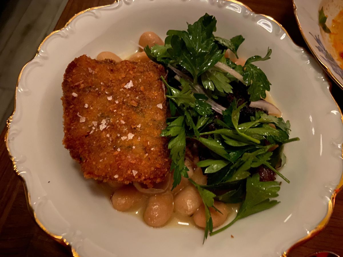 A crispy pig’s head with parsley salad and beans in a white bowl.