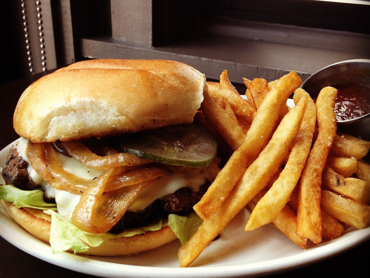 A burger topped with lettuce, pickles, cheese, and onions sits on a white plate with a side of fries and ketchup.