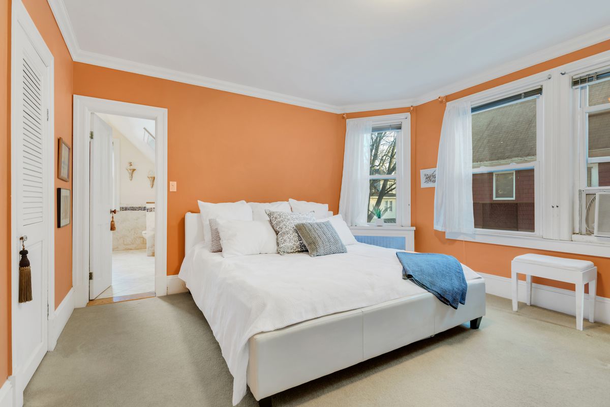 A bedroom with orange walls and several windows. 