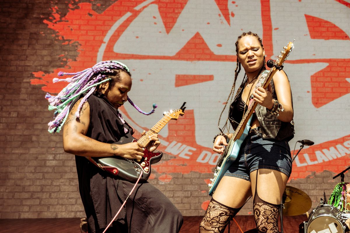 Two people with dreadlocks and black clothes playing guitar on stage.