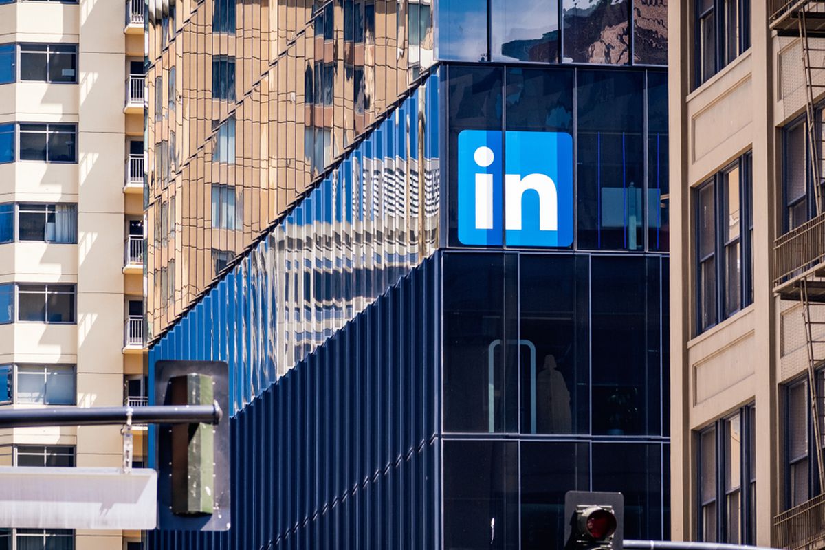 The LinkedIn logo—a blue square with the word “in” written in white”—on the side of a high-rise building with a black glass facade.