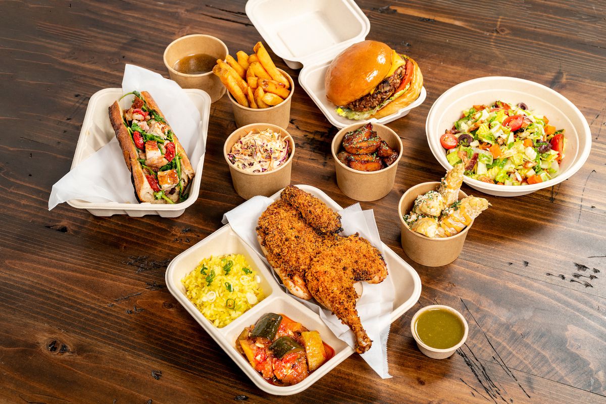 A tilted shot of food arranged on a wooden table, including chicken and sandwiches.