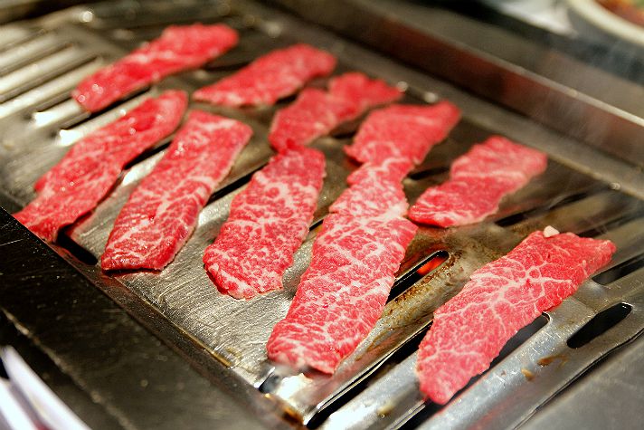 Raw pieces of thinly sliced beef at Park’s Barbeque on a steel tabletop grill.