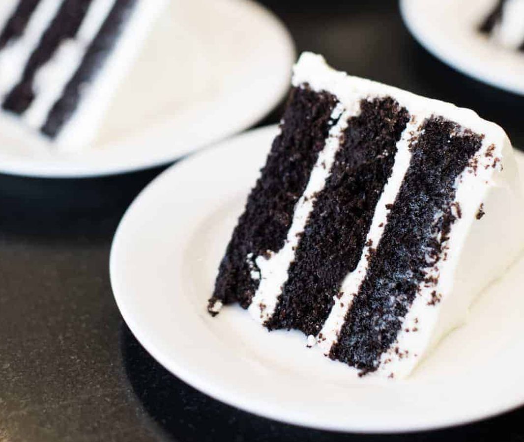 A slice of chocolate cake with vanilla frosting on a white plate. 