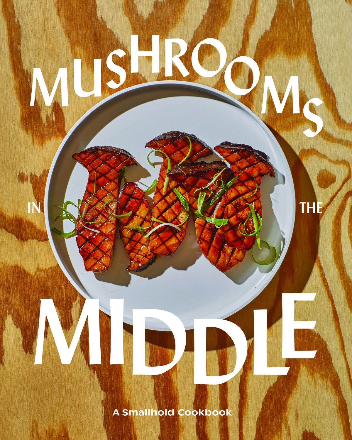 A plate with four seared mushrooms sit on a gray plate with white text of the image that reads “Mushrooms in the Middle.”