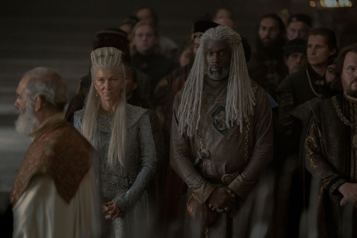 Rhaenys Targaryen stands next to her husband Corlys Velaryon among a crowd of people at court in House of the Dragon.