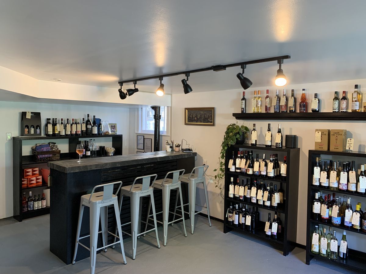 A black countertop bar with a few grey stools surrounded by shelves of wine.
