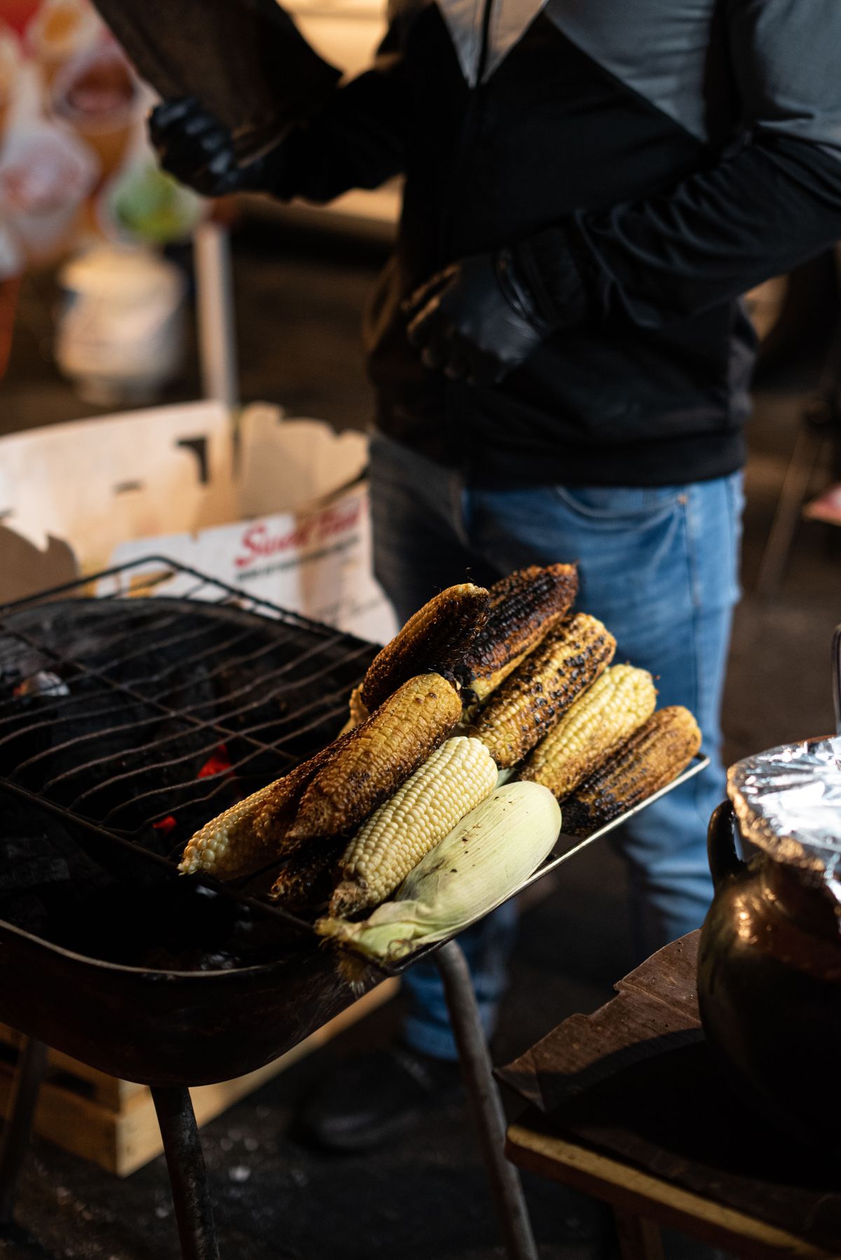 A street grill with stacked corn cobs ready for elote.