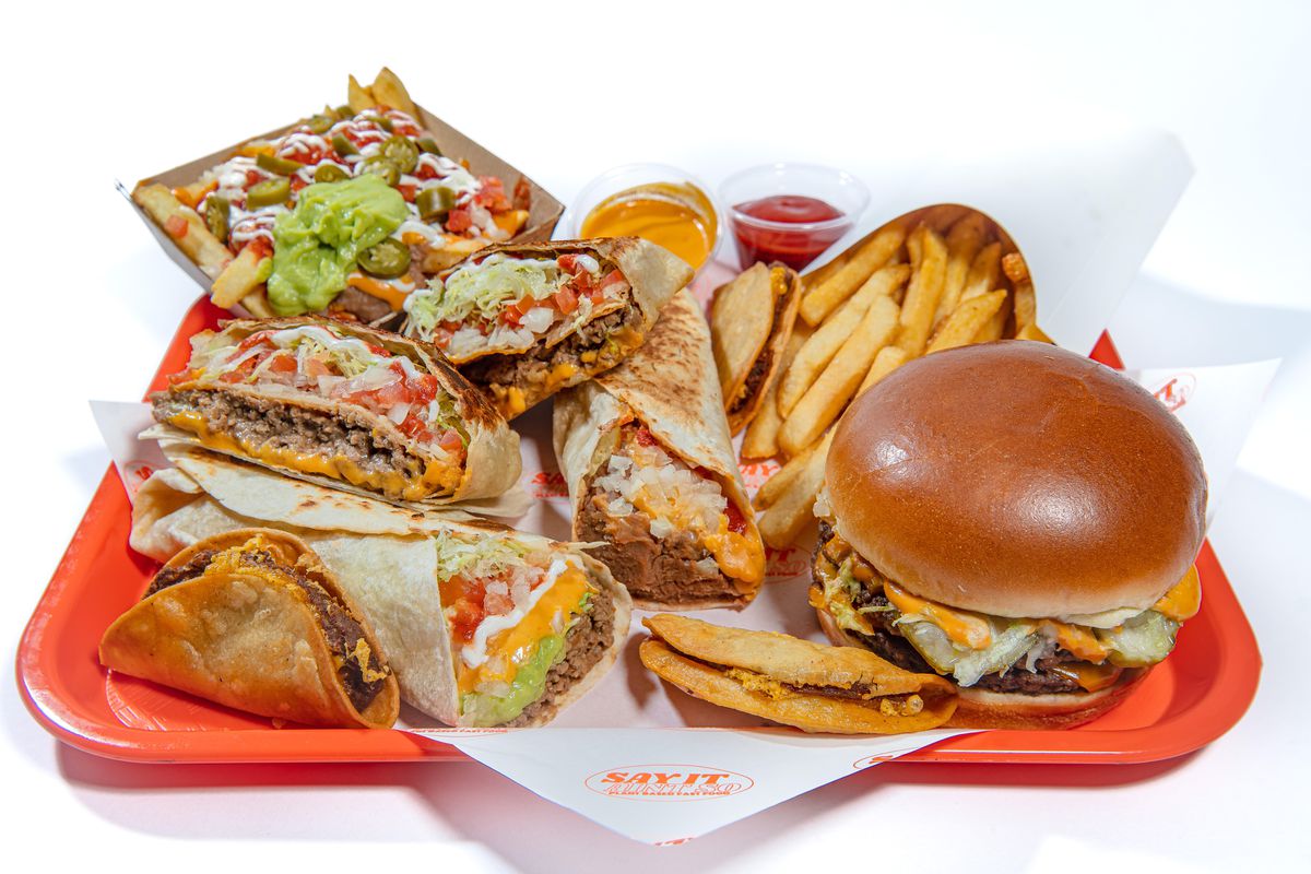 An orange tray holds a variety of vegan fast food, from burgers to fried sandwiches to french fries and tacos.