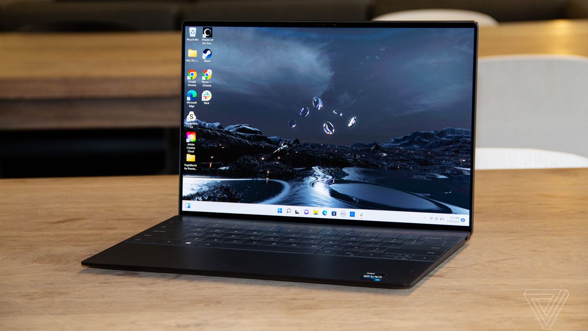 The Dell XPS 13 Plus open on a wooden table. The screen displays a river at night as a Windows desktop background.