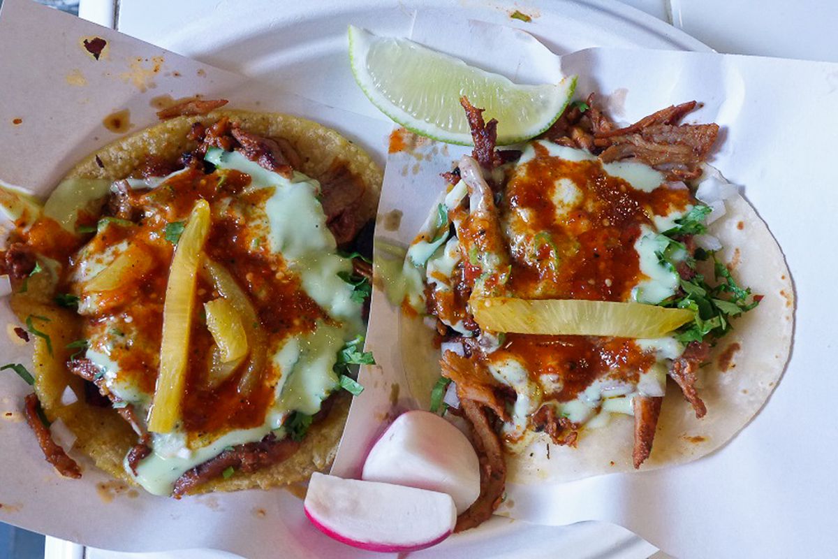 Two al pastor tacos from Los Tacos No. 1 with pineapple and red salsa in an overhead shot