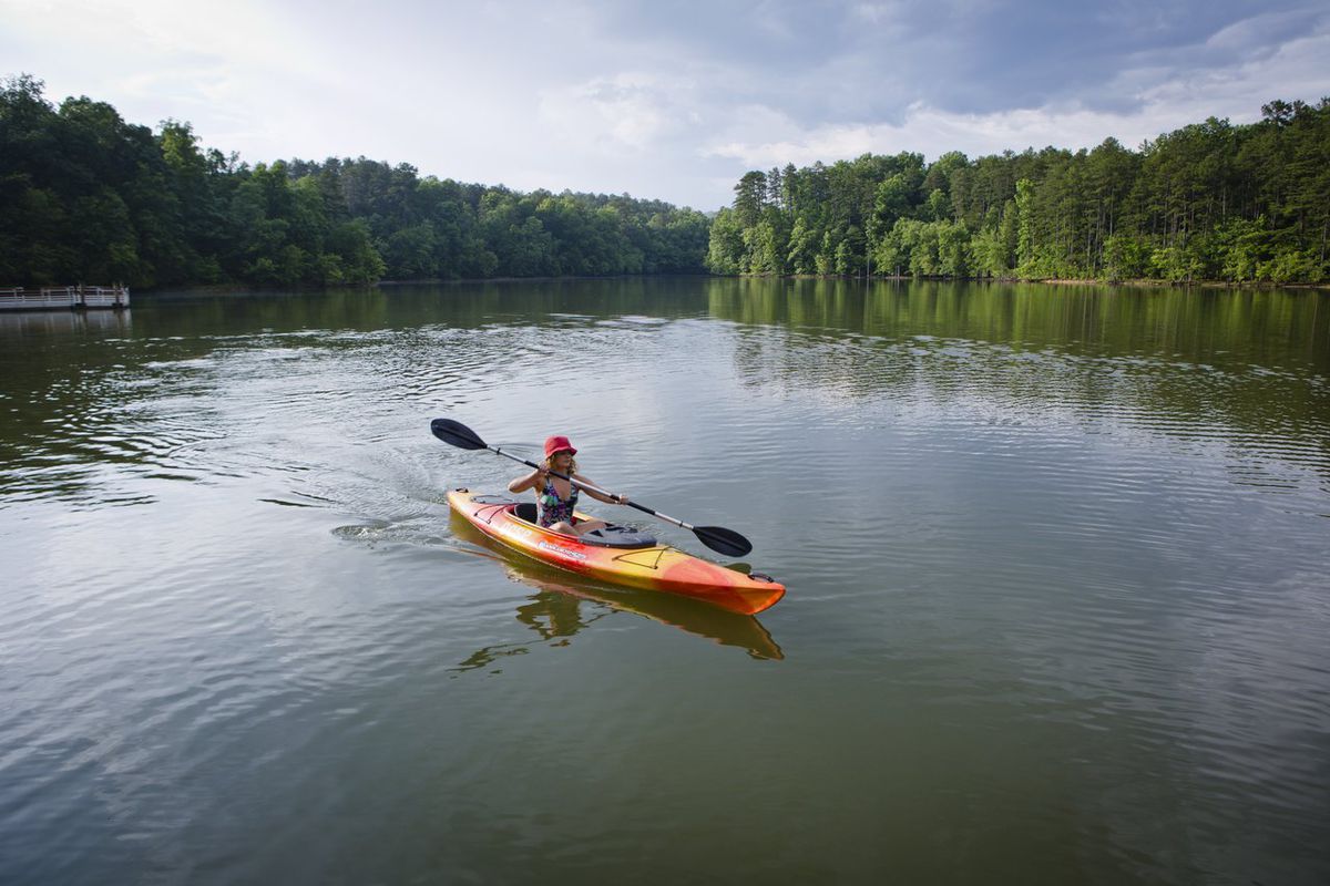 Female kayaker on a lake surrounded by trees. 