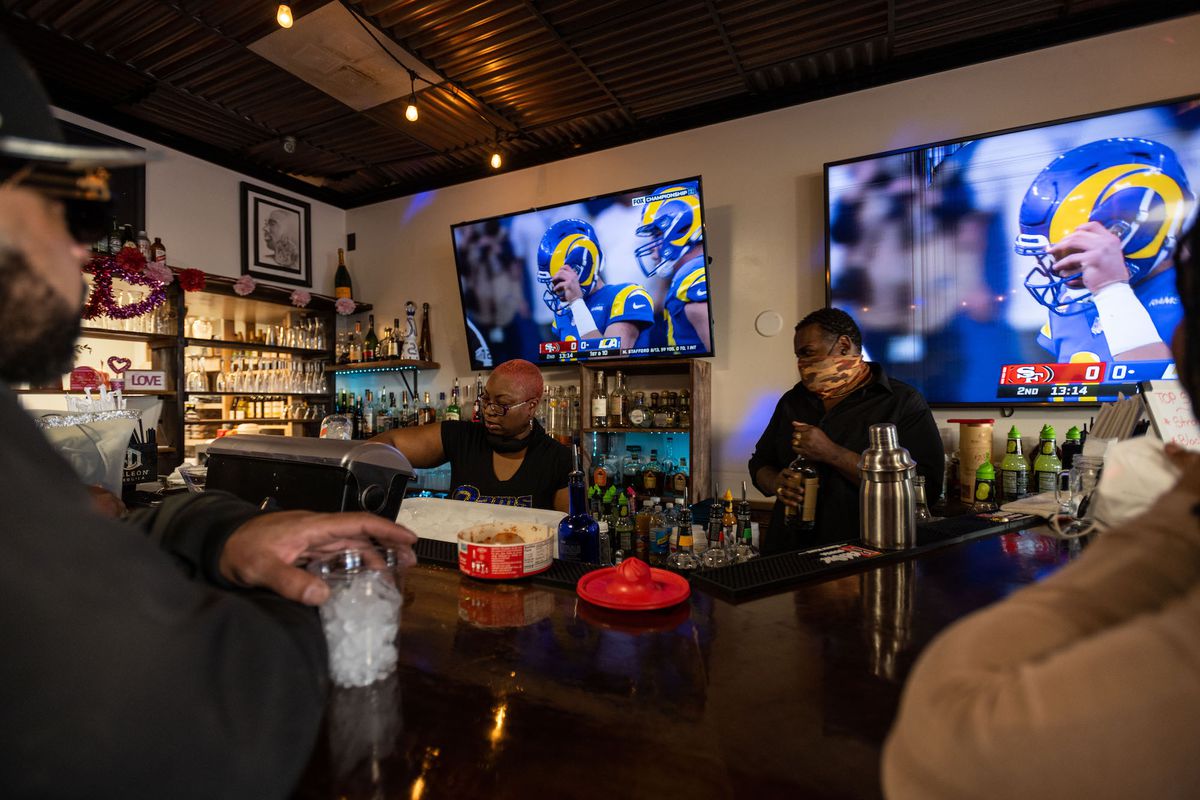 Two employees at a sports bar pour drinks during a game.