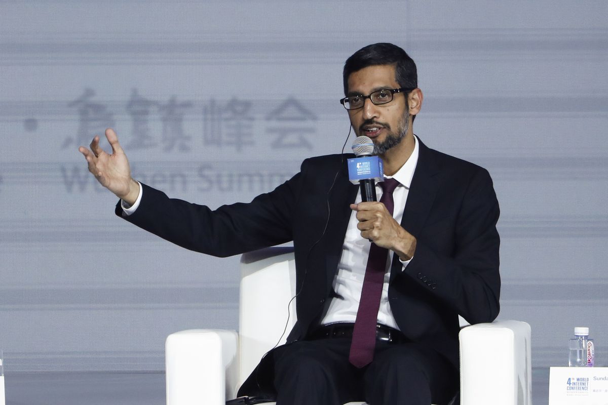 Google CEO Sundar Pichai, holding  microphone and gesturing while seated onstage